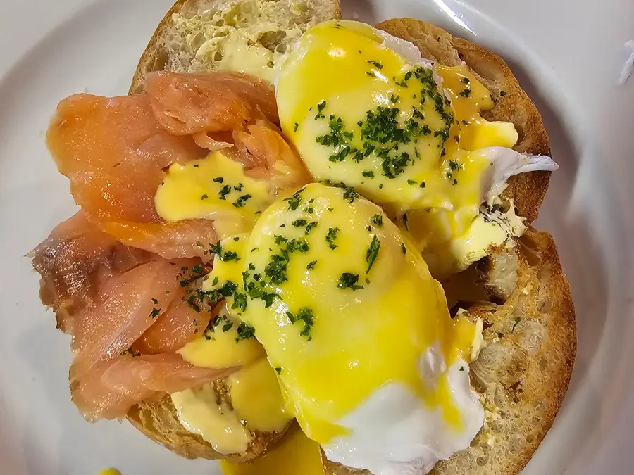 Eggs benedict with smoked salmon, hollandaise and chives on a white plate