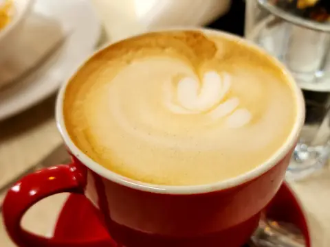 A flat white with latte art in a red cup and saucer